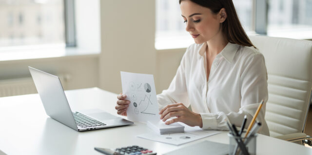 Consultante freelance travaillant dans un bureau lumineux devant un ordinateur, avec des documents financiers vierges et un tableau de trésorerie visuel soigneusement organisé.