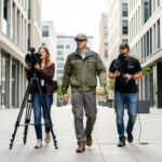 Une équipe de communication filme un agent de terrain dans un quartier urbain moderne, avec un cadrage dynamique et une lumière naturelle.